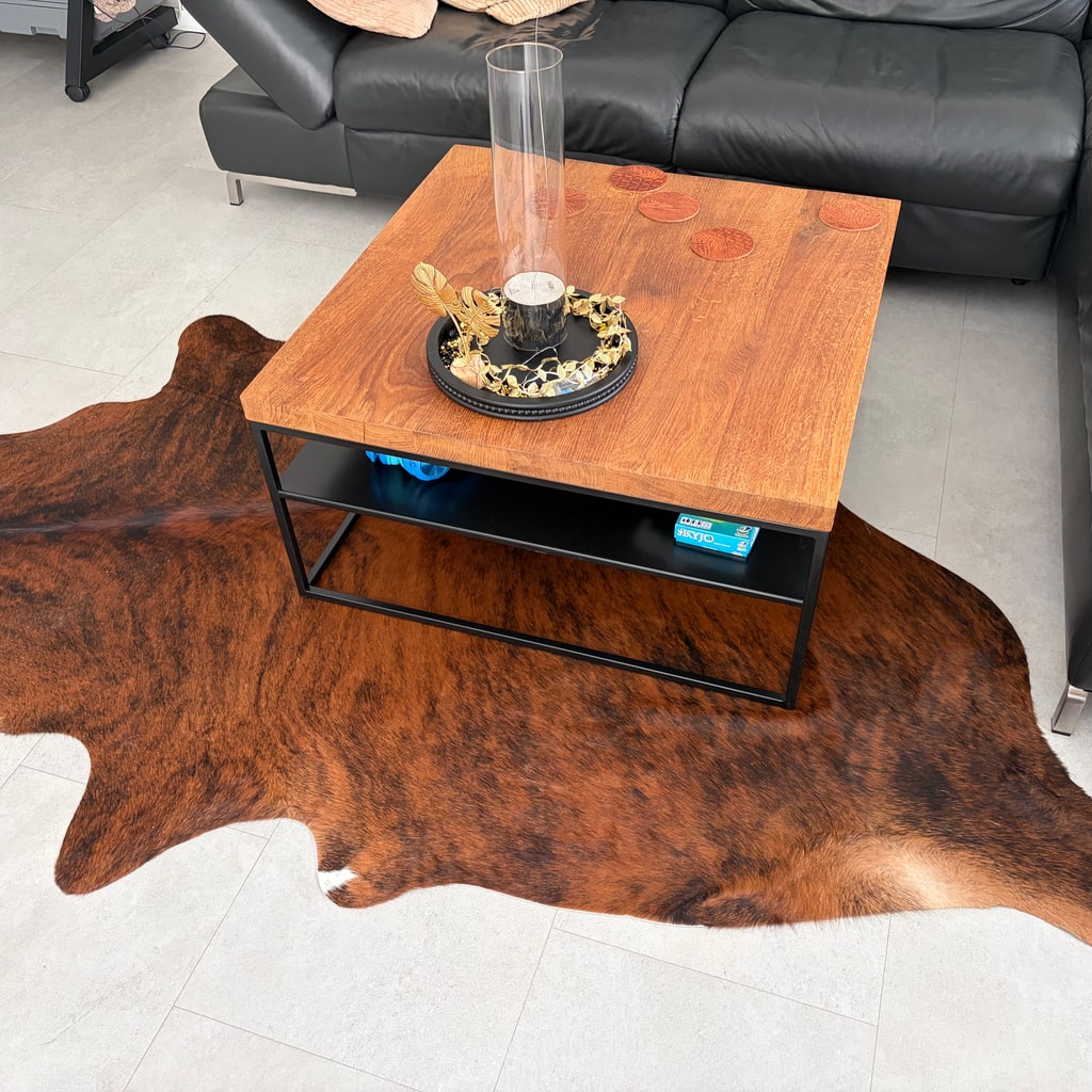 Peau de vache brune chinée sous une table basse dans un salon avec canapé en cuir noir.