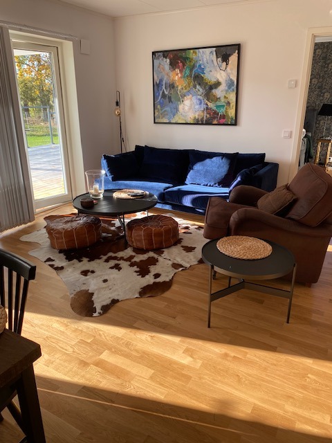 Peau de vache marron et blanche sous une table basse ronde noire et des poufs en cuir, près d’un canapé bleu sur un parquet.