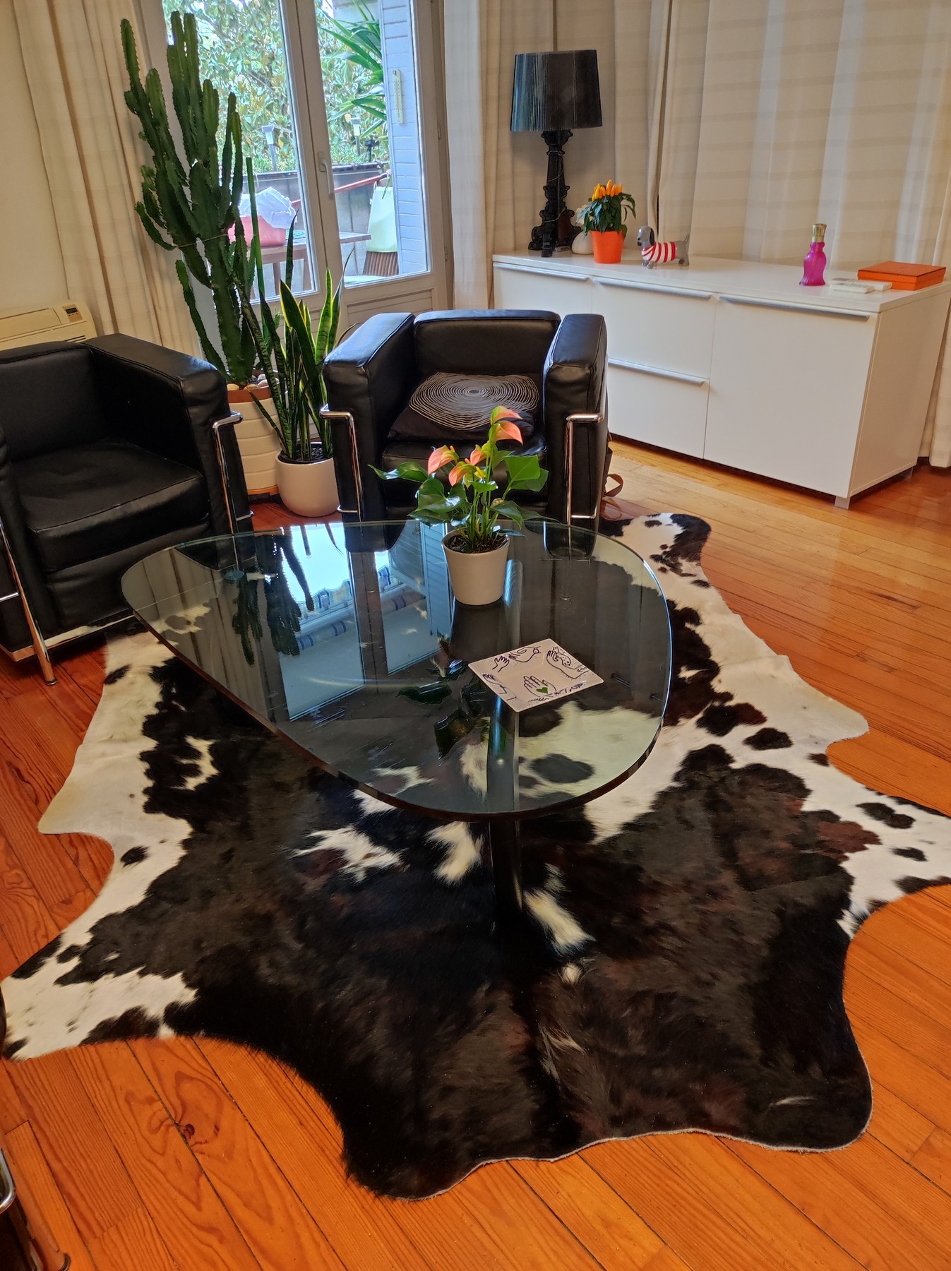 Peau de vache brune et blanche sous une table basse en verre, près de sièges en cuir noir