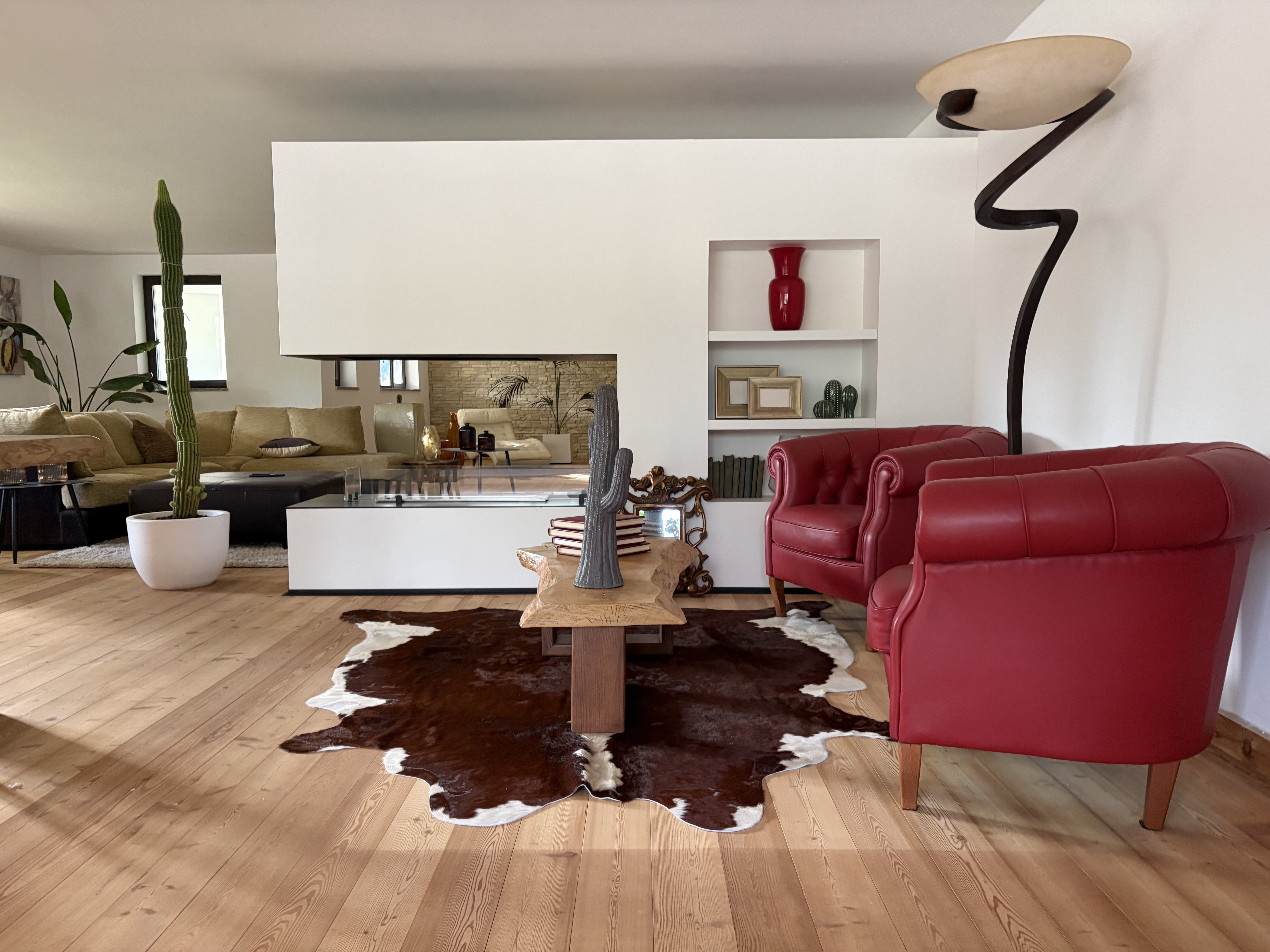 Peau de vache brune et blanche sous une table basse en bois, près de fauteuils rouges sur un parquet