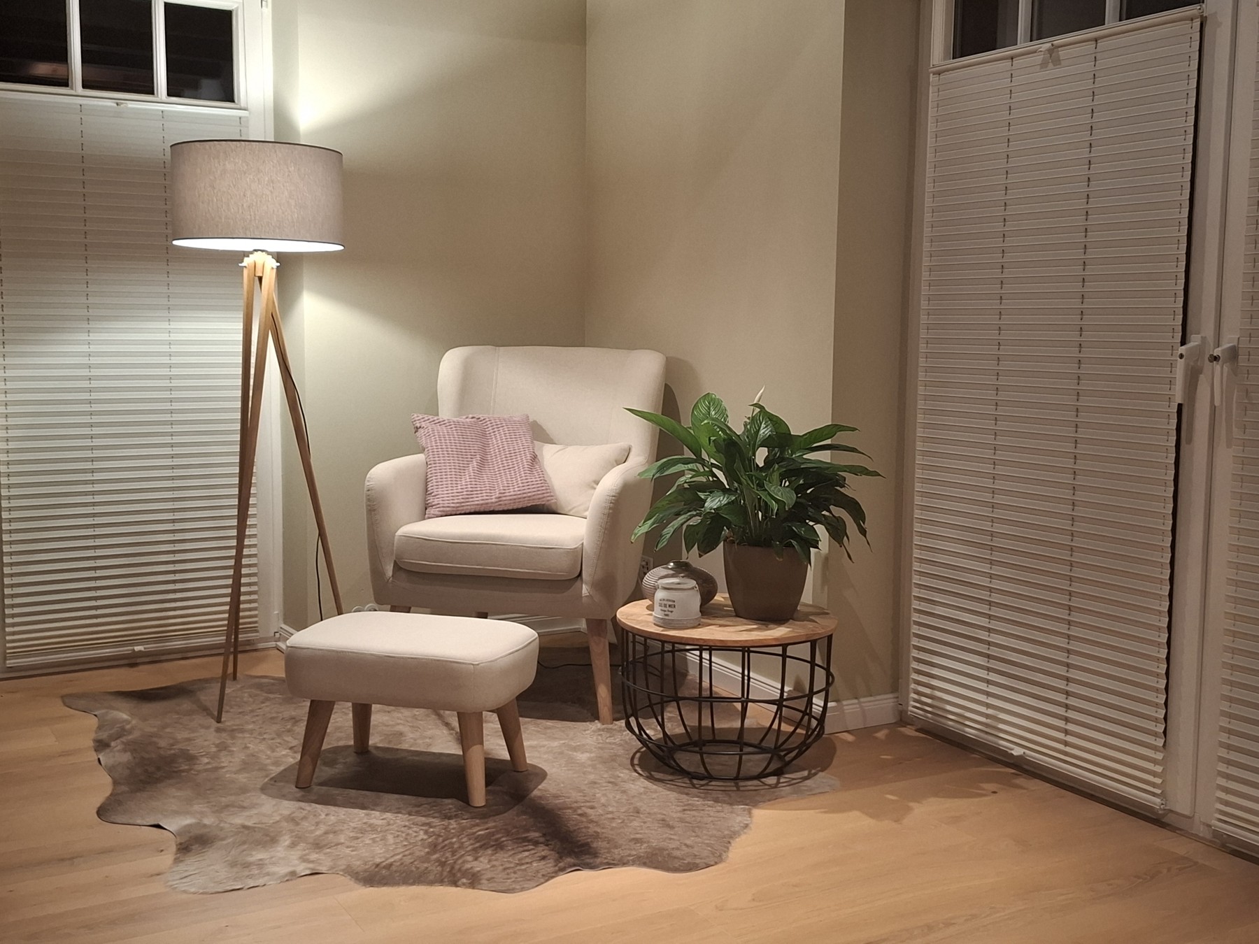 Peau de vache gris-brun sous un fauteuil beige et son repose-pieds, près d’un lampadaire et d’une table d’appoint