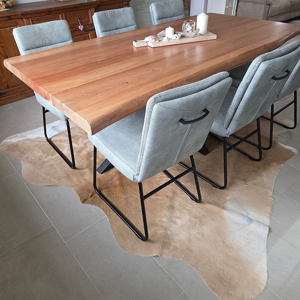 Peau de vache brun clair sous une grande table à manger en bois entourée de chaises grises.